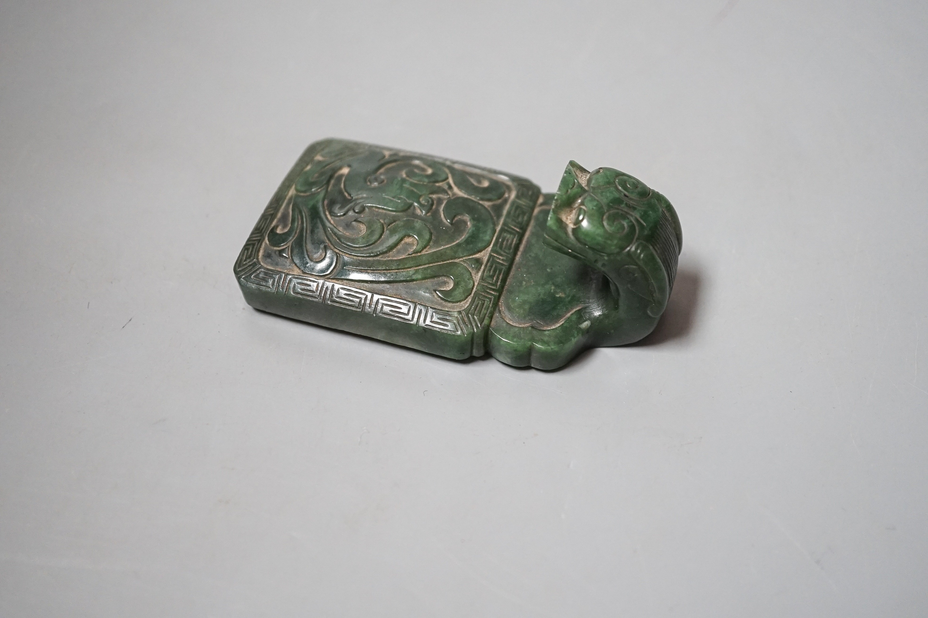 A Chinese spinach green jade belt hook, 19th century, in archaistic style, carved in relief with a chi-dragon, with a dragon head handle, 9cm
